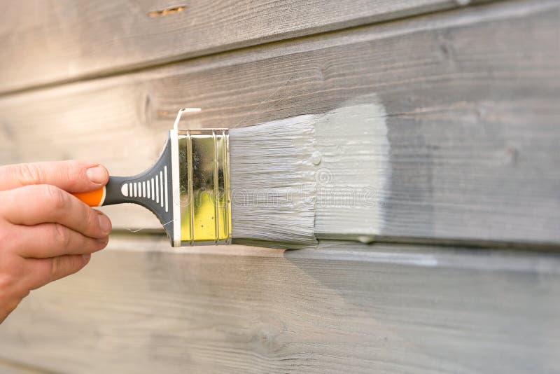 Kobieta pracownik maluje drewnianą domową zewnętrzną ścianę z paintbrush i drewnianym ochronnym kolorem