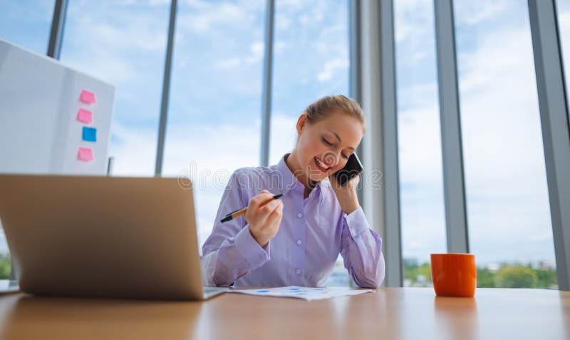 Kobieta pracuje na laptopie przy biurem podczas gdy opowiadający na telefonie, bizneswomanu portret fotografia stock Kobieta pracuje na laptopie przy biurem podczas gdy opowiadający na telefonie, bizneswomanu portret fotografia stock