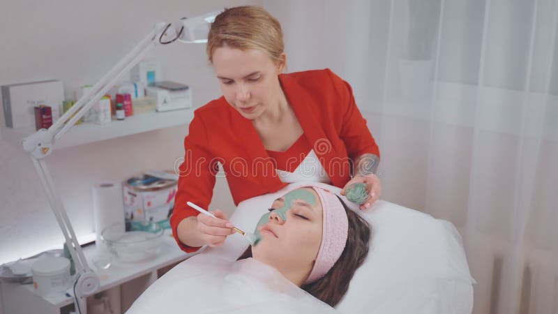 Kobieta relaksująca się w klinice kosmetologicznej profesjonalny estetyk przyklejający maskę kobiecej twarzy zdjęcie wideo