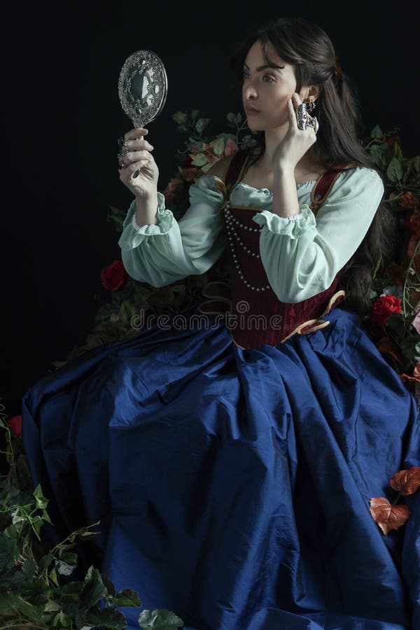 A Renaissance or Fantasy/fairytale/gypsy woman wearing a red brocade corset and blue silk skirt and looking in a silver mirror. A Renaissance or Fantasy/fairytale/gypsy woman wearing a red brocade corset and blue silk skirt and looking in a silver mirror