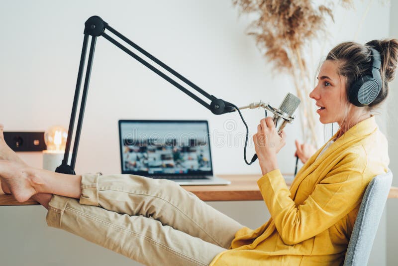 Kobieta siedzi z położeniem stóp na stole i nagrywaniem podkastów w jego małym przytulnym studio radiowym fotografia royalty free