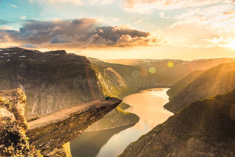02/09-17, Trolltunga, Norway. A woman is sitting on the edge of trolltunga facing the sun. The drop down is 700 m. 02/09-17, Trolltunga, Norway. A woman is sitting on the edge of trolltunga facing the sun. The drop down is 700 m