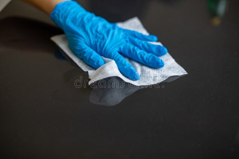 Kobieta sprzątająca powierzchnię stołu w biurze domowym z mokrymi chusteczkami w niebieskich rękawiczkach ze zdjęciem