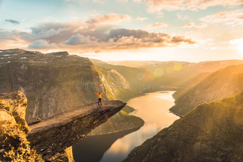 02/09-17, Trolltunga, Norway. A woman is standing on the edge of trolltunga with her side against the sun. The drop down is 700 m. 02/09-17, Trolltunga, Norway. A woman is standing on the edge of trolltunga with her side against the sun. The drop down is 700 m