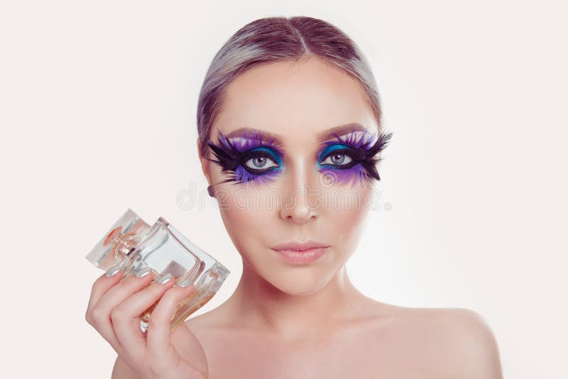 Kobieta trzyma pokazywać pachnidłu srebną biżuterię na głowie z artystycznym purpurowym niebieskiego oka makeup piórkiem na rzęsa zdjęcie stock