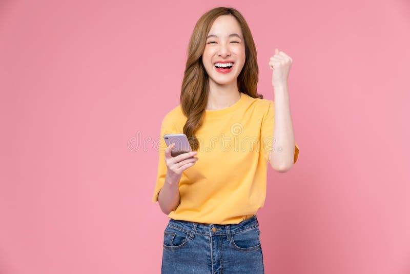 Kobieta trzymająca smartfon z pięściami świętowała zwycięstwo, wyrażając sukces na jasnym różowym tle. zdjęcia stock