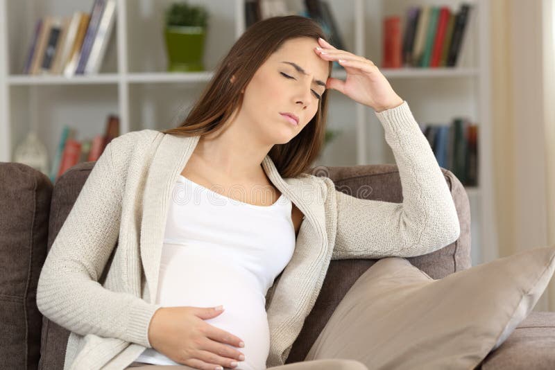 Pregnant woman suffering migraine sitting on a sofa at home. Pregnant woman suffering migraine sitting on a sofa at home