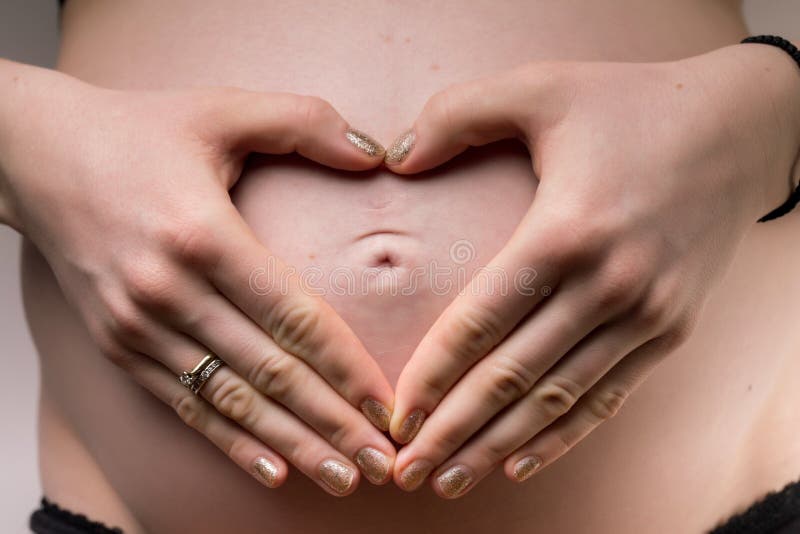 Kobieta W Ciąży trzyma jej ręki w kierowym kształcie na jej dzieci bu