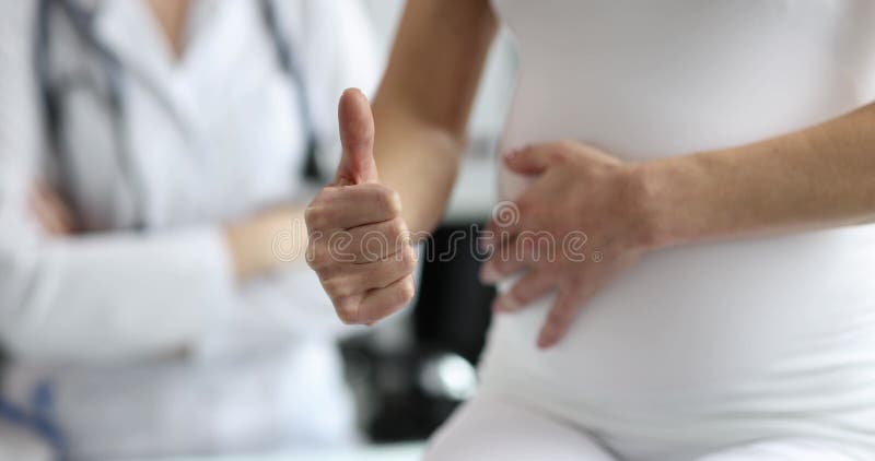 Kobieta w ciąży uderza brzuchem i pokazuje kciuki