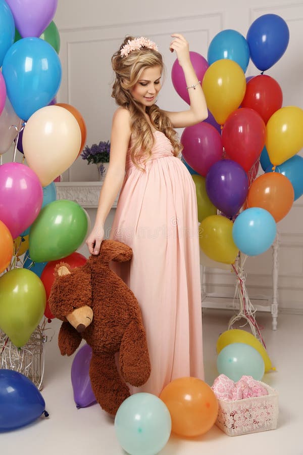 Fashion interior photo of beautiful pregnant woman with long blond hair in elegant dress, with a lot of colorful air balloons. Fashion interior photo of beautiful pregnant woman with long blond hair in elegant dress, with a lot of colorful air balloons