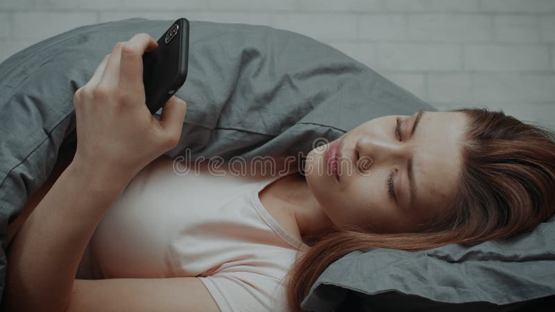 Kobieta w depresji przy użyciu smartfona leżącego w łóżku w domu