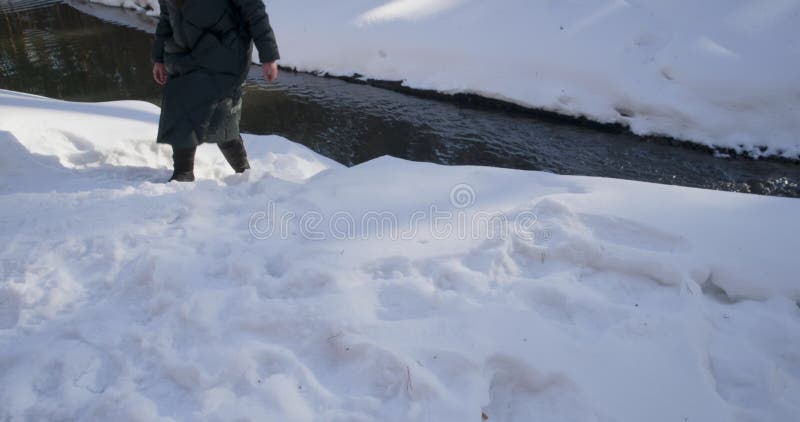 Kobieta w kurtce chodząca zimą koło rzeki na śnieżnych nogach brzegowych blisko rzeki.