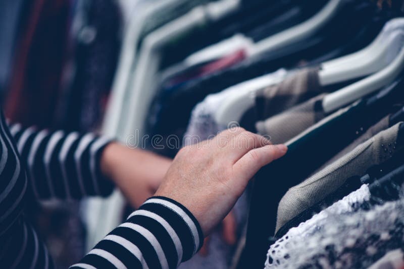 Kobieta wyszukuje przez odzieży przy drugi ręki ulicznym rynkiem zdjęcie stock Kobieta wyszukuje przez odzieży przy drugi ręki ulicznym rynkiem zdjęcie stock