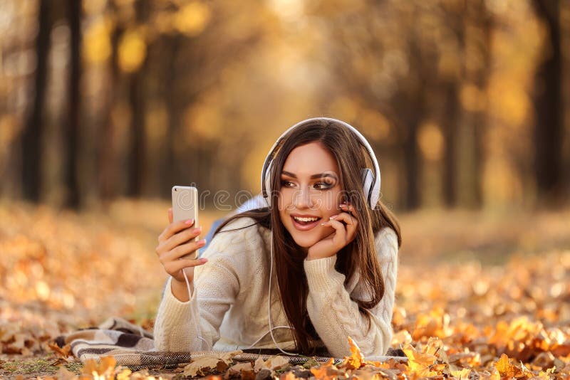 Beautiful woman with headphones and smartphone lying on the ground in autumn park. Beautiful woman with headphones and smartphone lying on the ground in autumn park