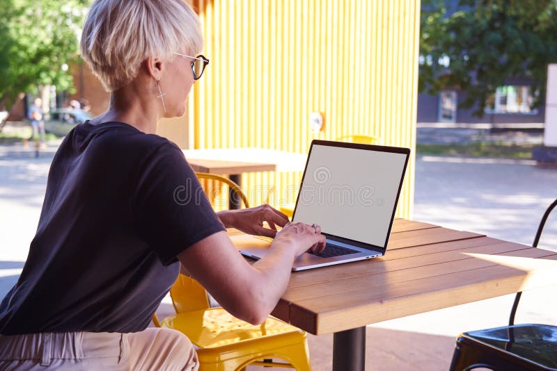 Kobieta z krótką fryzurą pracująca na laptopie, przestrzeń na ekranie do projektowania Siedzi na dworze w żółtej nowoczesnej kawi zdjęcie stock Kobieta z krótką fryzurą pracująca na laptopie, przestrzeń na ekranie do projektowania Siedzi na dworze w żółtej nowoczesnej kawi zdjęcie stock