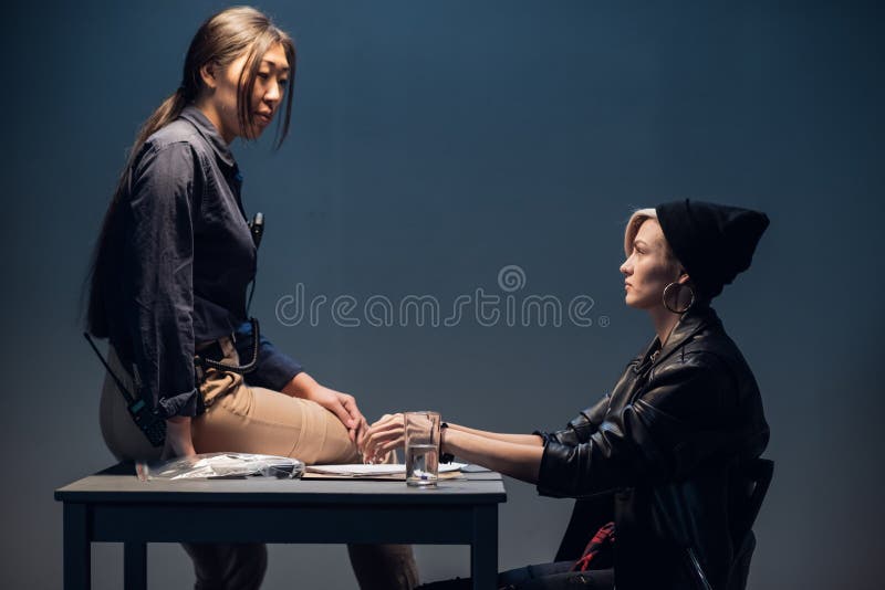 A female investigator sits on a table and interrogates a young criminal in an interrogation room. A female investigator sits on a table and interrogates a young criminal in an interrogation room.