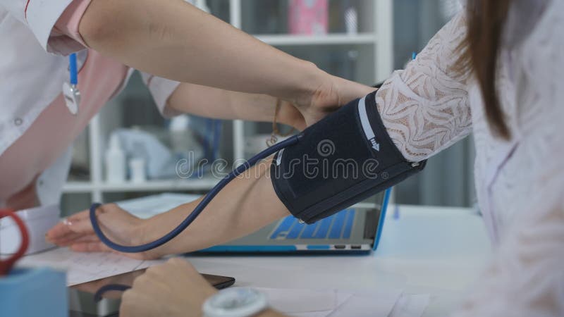 Kobiety lekarka mierzy naciska pacjent w biurze przy kliniką i pisze jej przydziale, w górę