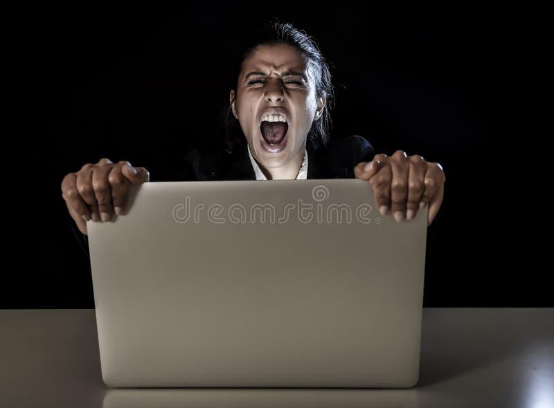 Young business woman or student girl working in darkness on laptop computer late at night holding the screen angry in stress and upset in long hour of work concept isolated on black background. Young business woman or student girl working in darkness on laptop computer late at night holding the screen angry in stress and upset in long hour of work concept isolated on black background