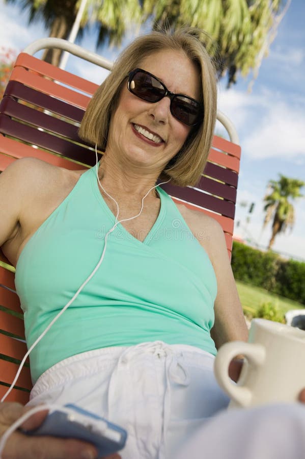 Woman lying on sunlounger listening to portable music player portrait. Woman lying on sunlounger listening to portable music player portrait.