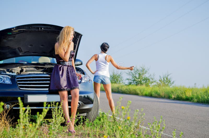 Women hitchhiking after a breakdown with their car pulled to the side of a country road with the hood up. Women hitchhiking after a breakdown with their car pulled to the side of a country road with the hood up