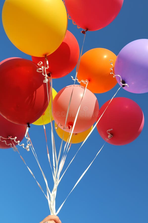 Woman`s hand holding bunch of multicolored balloons in the city festival on blue sky background, vertical composition. Woman`s hand holding bunch of multicolored balloons in the city festival on blue sky background, vertical composition