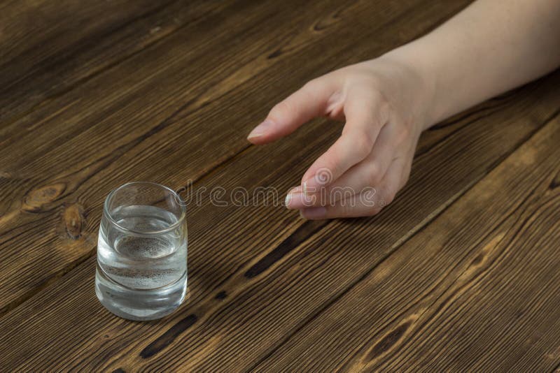 Kobiety ` s ręka dosięga dla szkła z alkoholem, drewniany tło, zakończenie, upiorny alkoholizm zdjęcia stock Kobiety ` s ręka dosięga dla szkła z alkoholem, drewniany tło, zakończenie, upiorny alkoholizm zdjęcia stock