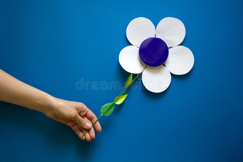 Kobiety ` s ręki trzyma papierowych kwiaty z kruszcowym kremowym słoju zbiornikiem na błękitnego papieru tle papieru cięcie obrazy stock Kobiety ` s ręki trzyma papierowych kwiaty z kruszcowym kremowym słoju zbiornikiem na błękitnego papieru tle papieru cięcie obrazy stock