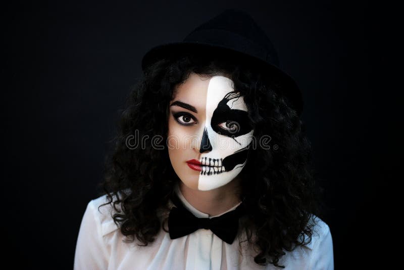 Creative woman with make-up for the Halloween party. The original idea for Halloween black and white skull on face, half of the image. Professional art portrait near black wall, free place horizontal. Creative woman with make-up for the Halloween party. The original idea for Halloween black and white skull on face, half of the image. Professional art portrait near black wall, free place horizontal