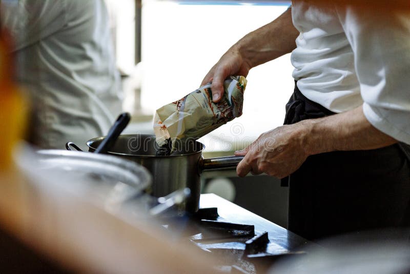 Koch kocht in einer Restaurantk?che, bespr?ht Gew?rze in die Wanne lizenzfreies stockbild Koch kocht in einer Restaurantk?che, bespr?ht Gew?rze in die Wanne lizenzfreies stockbild