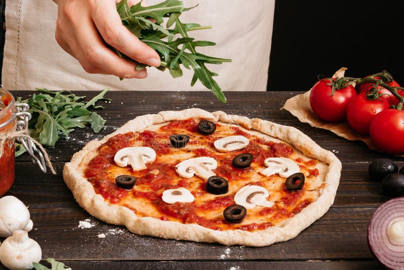 Kochen der Pizza Hände, die frischen Arugula Pizza hinzufügen Pizzabestandteile auf dem Holztisch lizenzfreies stockbild Kochen der Pizza Hände, die frischen Arugula Pizza hinzufügen Pizzabestandteile auf dem Holztisch lizenzfreies stockbild