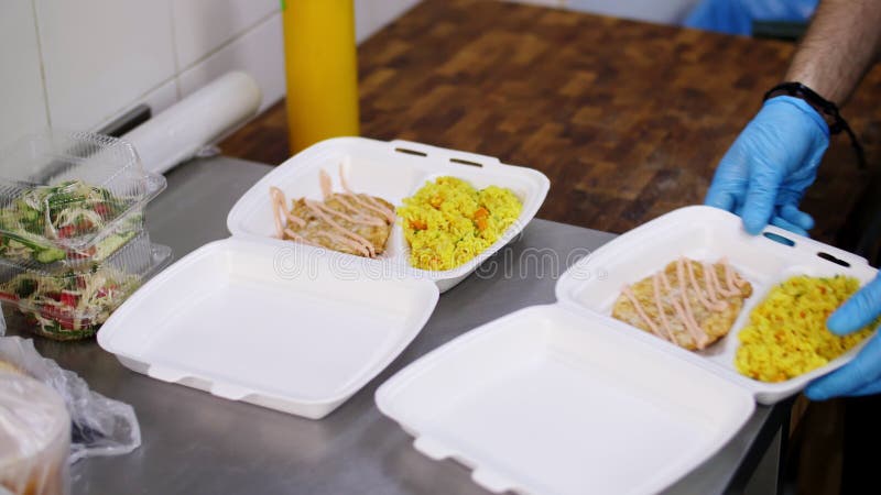 Kochen. Nahaufnahmefreiwilliger in den Schutzhandschuhen Verpackung freie warme Mahlzeiten in den an die Armen zu liefernden Lunch