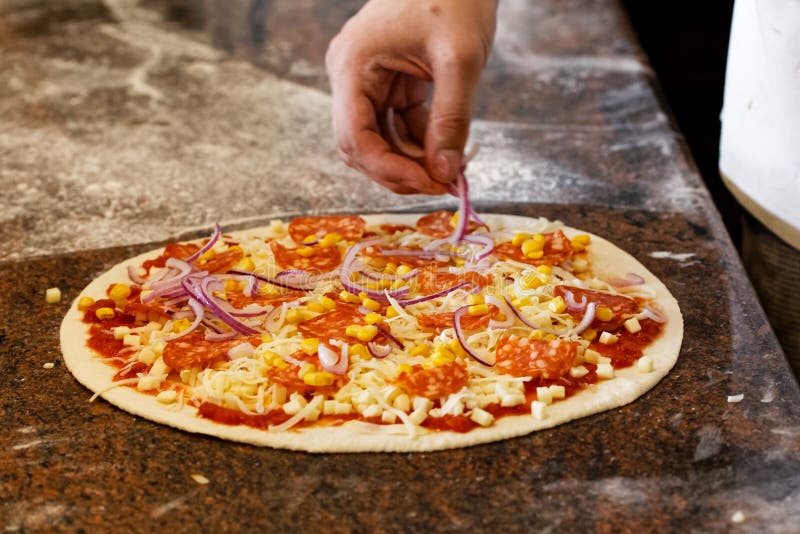 Kochen Sie ` s Hände, die rote Zwiebel auf Tomatenbasispizza setzen lizenzfreie stockbilder Kochen Sie ` s Hände, die rote Zwiebel auf Tomatenbasispizza setzen lizenzfreie stockbilder