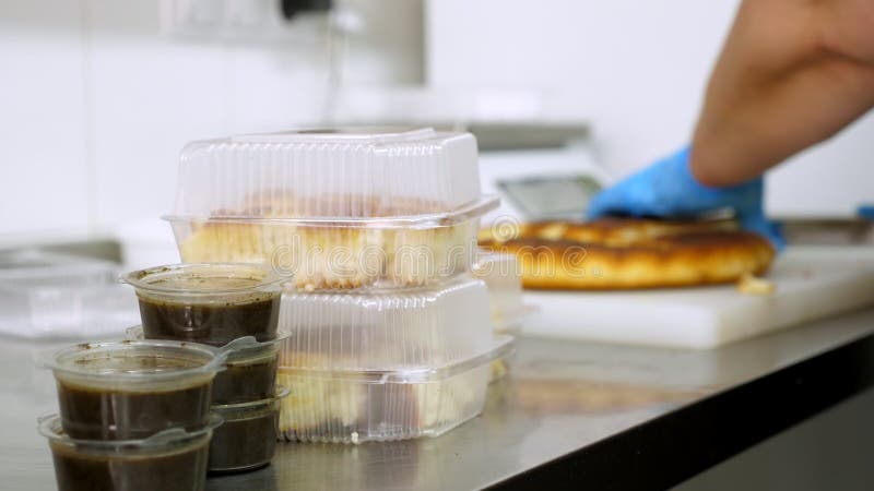 Kochen. Verpackung freiwillige Küchearbeitskraft der Nahaufnahme in den Schutzhandschuhen freies geschnittene Brot in den Lunchbox