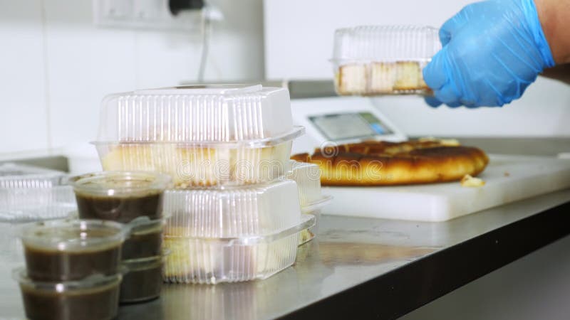 Kochen. Verpackung freiwillige Küchearbeitskraft der Nahaufnahme in den Schutzhandschuhen freies geschnittene Brot in den Lunchbox