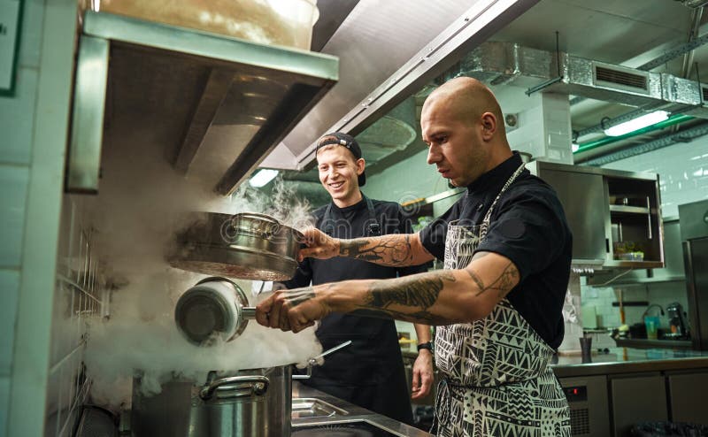 Kochschule Hübscher und überzeugter Chef, der wie man seine zwei Assistenten in einer Restaurantküche unterrichtet, kocht