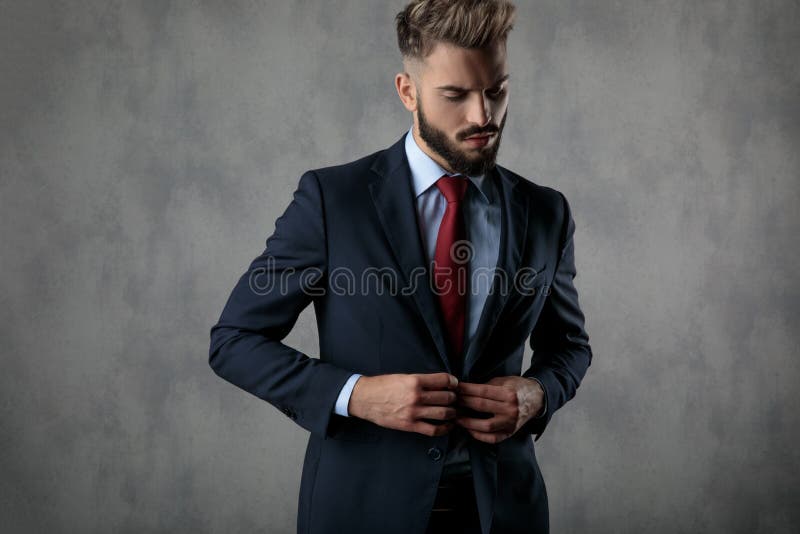 Koele sexy jonge zakenman die zijn kostuum en blikken neer dichtknopen