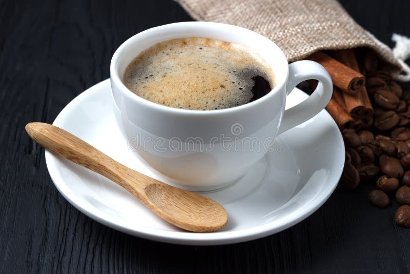 Koffie in een witte kop met een schotel en een houten lepel op een zwarte achtergrond met een zak van koffiebonen stock afbeeldingen Koffie in een witte kop met een schotel en een houten lepel op een zwarte achtergrond met een zak van koffiebonen stock afbeeldingen