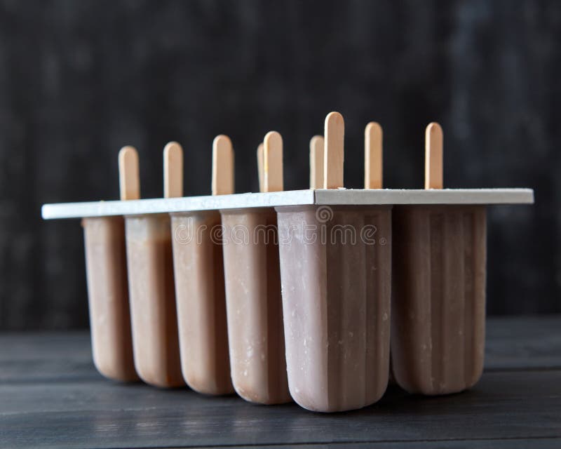 Koffieroomijs op een stok in plastic vormen op een donkere houten achtergrond De zomerdessert stock foto Koffieroomijs op een stok in plastic vormen op een donkere houten achtergrond De zomerdessert stock foto