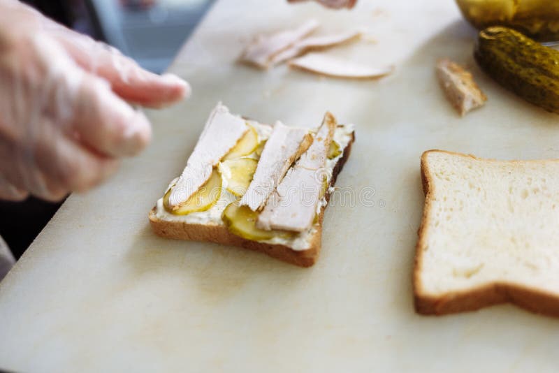 Kok die in polyethyleenhandschoenen een sandwich op een witte raad maken royalty-vrije stock foto's Kok die in polyethyleenhandschoenen een sandwich op een witte raad maken royalty-vrije stock foto's