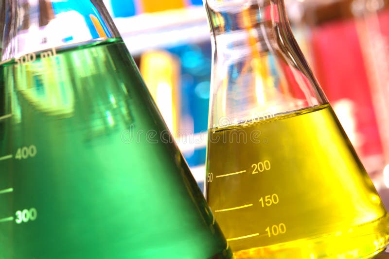 Laboratory glass conical Erlenmeyer flasks filled with yellow and green chemical liquid for an experiment in a science research lab. Laboratory glass conical Erlenmeyer flasks filled with yellow and green chemical liquid for an experiment in a science research lab