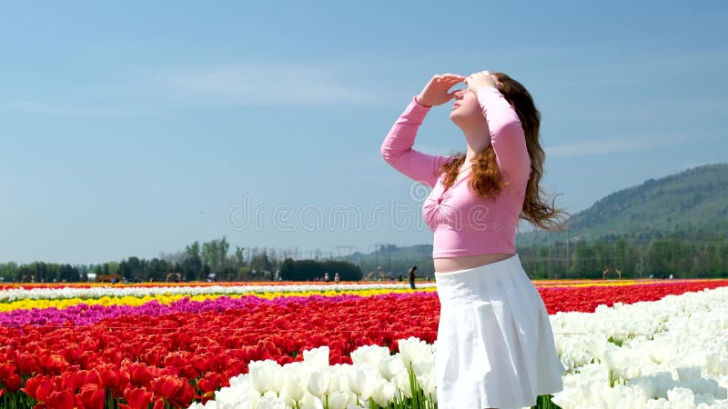 Kolekcja filmów i zdjęć, gdzie dziewczyna w białej spódniczce spaceruje po polu z tulips blue background sky