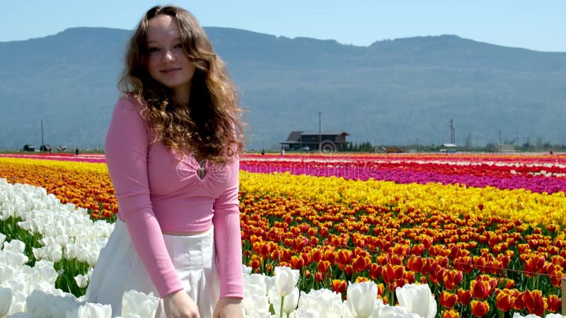 Kolekcja filmów i zdjęć, gdzie dziewczyna w białej spódniczce spaceruje po polu z tulips blue background sky