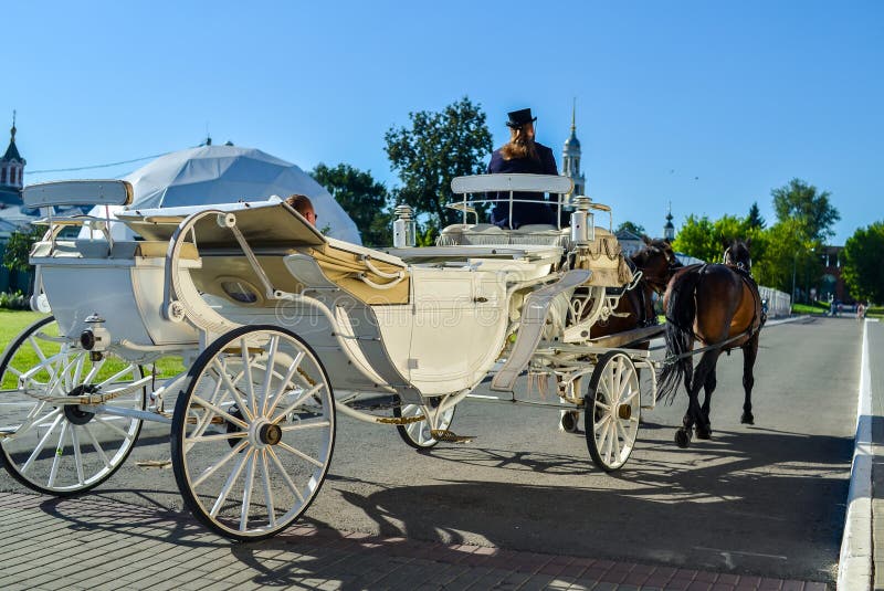 Kolomna Ryssland - Augusti 11, 2018 Elegant vit vagn med kuskar i svart hatt och bruna hästar som bär turister arkivbilder Kolomna Ryssland - Augusti 11, 2018 Elegant vit vagn med kuskar i svart hatt och bruna hästar som bär turister arkivbilder