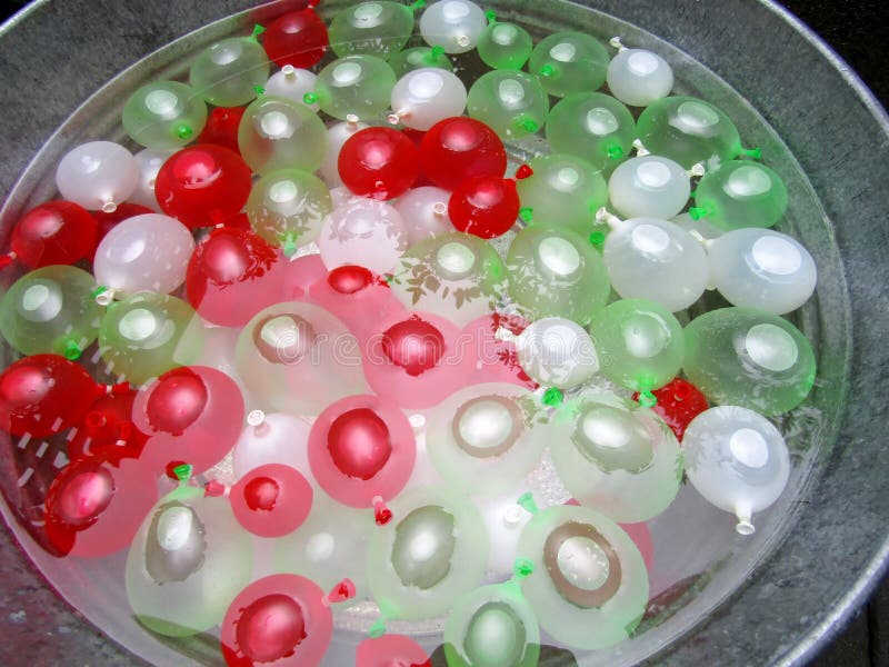 White, red and green mini water balloons in water to prevent popping. White, red and green mini water balloons in water to prevent popping