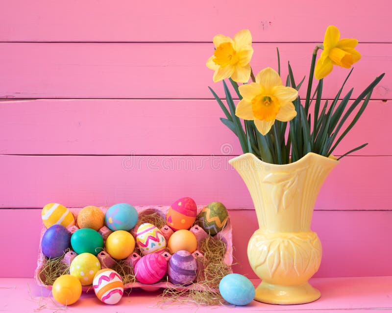 Kolorowi Wielkanocni jajka w kartonie z rocznik Żółtą wazą wypełniającą z wiosen Daffodils przeciw Jaskrawemu Różowemu drewnu Wsi