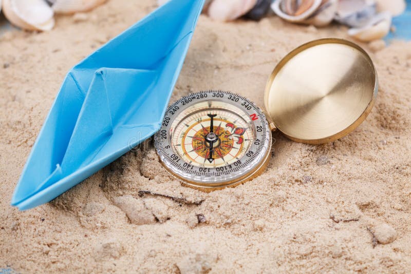 Kompas en papieren bootje in het zand stock fotografie