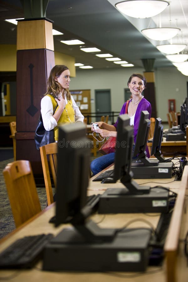 Two young female college students standing next to computers in school library. Two young female college students standing next to computers in school library