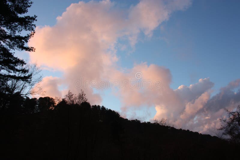 Komt in de avond aan de zonsondergang kleurt de duidelijke blauwe hemel en de roze en zalmwolken de heuvels worden donker en zwar royalty-vrije stock foto's Komt in de avond aan de zonsondergang kleurt de duidelijke blauwe hemel en de roze en zalmwolken de heuvels worden donker en zwar royalty-vrije stock foto's