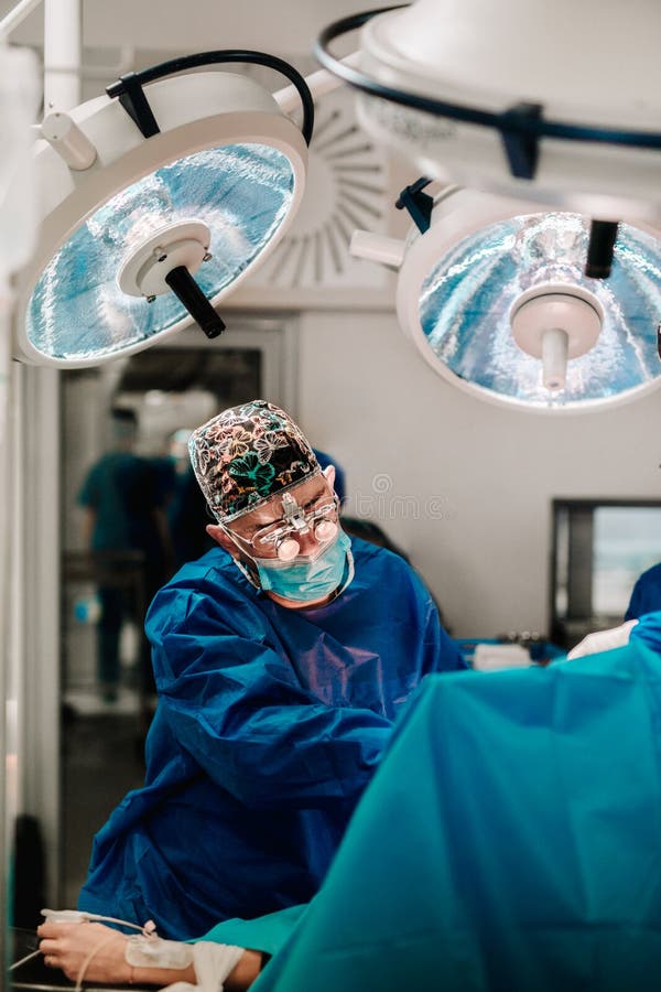 Koncentrerad kirurg och lag som fungerar en patient i en operationteater Kirurg som bär kirurgisk hjälmsystemblixt arkivfoto Koncentrerad kirurg och lag som fungerar en patient i en operationteater Kirurg som bär kirurgisk hjälmsystemblixt arkivfoto
