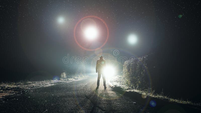 Koncepcja ufo. świecące orbiny unoszące się nad mglistą drogą w nocy. z sylwetką patrzącą na światła obrazy stock